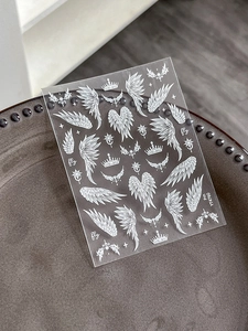 Macro shot of white angel wings and crown nail stickers on transparent adhesive film