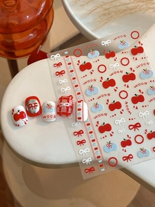 Detail of red apple and white bow embossed nail stickers with finished manicure display
