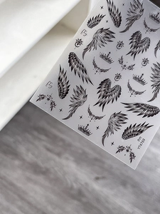 Macro shot of wing and crown nail art decals with black line drawing patterns