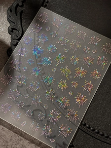 Macro view of holographic laser firework nail stickers showing rainbow shine on dark surface