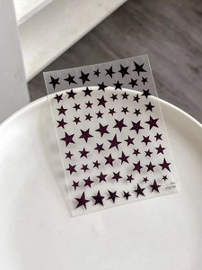 Detail of dark purple star nail art stickers with glitter finish on white tray
