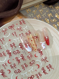 Détail de stickers à ongles nœuds et perles sur ongles longs rouges et dorés brillants