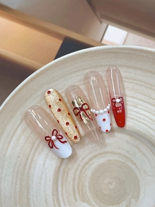 Vue détaillée de nail art avec nœuds rouges 3D, perles et touches dorées
