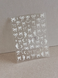Détail d'autocollants 3D blancs pour ongles avec motifs de nœuds, étoiles et lunes