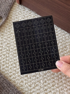 Close-up of YT85 gold cross and star nail art stickers held against a cozy background