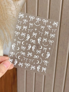 Détail d'autocollants gaufrés blancs pour ongles avec nœuds, étoiles et perles