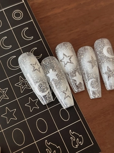 Detail of silver glitter fake nails with white star and moon patterns on a black display card