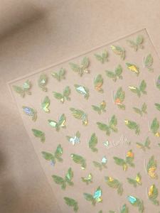 Close-up of iridescent green butterfly nail art stickers with laser holographic effects