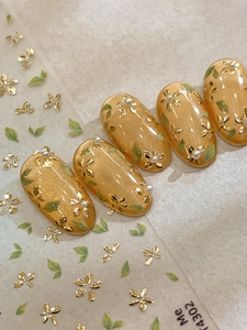 Detail of amber nail stickers with gold foil flowers, green leaves and small white pearls