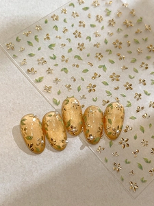 Detail of 3D gold floral nail stickers with green leaves on cat-eye nails with pearls