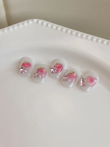 Dettaglio di unghie finte rosa con fragole e cuori e strass 3D su un vassoio di ceramica