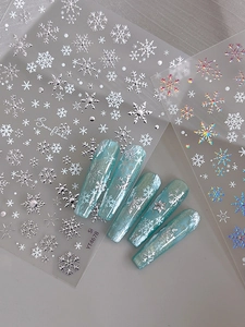 Macro detail of holographic snowflake nail stickers with silver glitter accents and blue finish