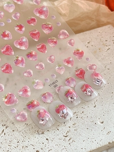 Dettaglio di adesivi per nail art fragola e cuore con texture 3D su unghie bianche