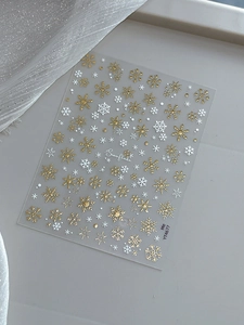 Detailed view of gold and white snowflake nail art stickers with metallic texture finish