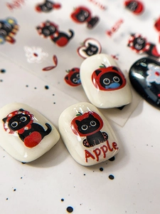 Detail view of 3D embossed black cat and red apple nail stickers on sample tips