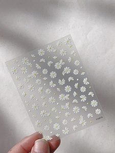 Macro detail of embossed daisy nail art stickers with white petals and yellow centers