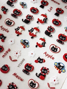 Detail of 3D embossed nail stickers featuring black cats and red apples with glitter accents
