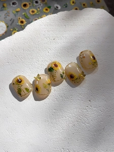 Detail of sunflower press-on nails with 3D butterfly gold accents on white stone