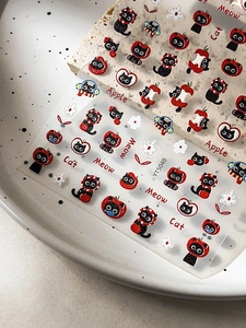 Close-up of cute black cat and red apple embossed nail art stickers on a textured stone