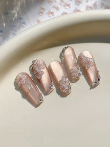 Macro shot of embossed white floral nail stickers on pink cat-eye gel press-on nails