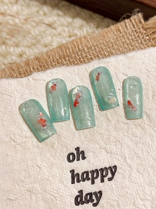 Macro detail of handmade press-on nails featuring red goldfish designs and shell accents