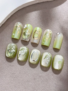 Gros plan d'ongles faits main muguet vert avec des papillons argentés en relief 3D