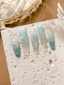 Macro view of long almond press-on nails with blue gradient, white flowers, and 3D details