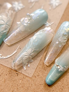 Detail of 3D embossed white floral nail stickers with pearl accents on blue base