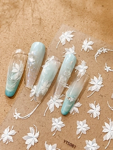 Close-up of 5D white floral embossed nail stickers on light blue gradient nails