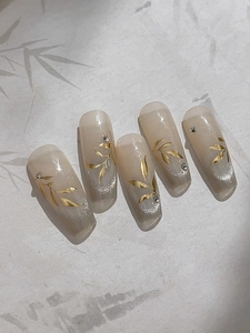 Vue détaillée de faux ongles dégradés nude avec motifs de feuilles dorées et strass