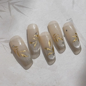 Faux ongles élégants avec motif de feuilles dorées et dégradé nude sur fond beige