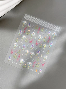 Detailed shot of iridescent bow and shell-light flower nail art stickers on a textured base