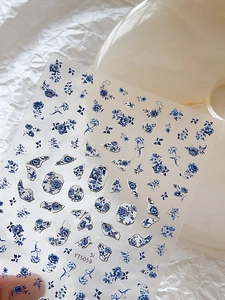 Detailed close-up of blue and white porcelain floral nail stickers on a textured background