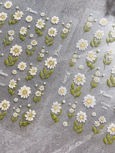 Macro detail of 3D embossed white daisy nail stickers with green leaves and pearl texture