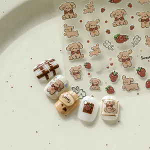 Détails d'autocollants pour ongles ours et fraise sur des manucures crème et caramel