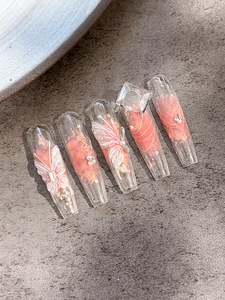 Close-up of pink coffin press-on nails with 3D butterfly, pearls and sequins