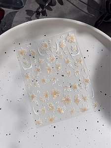 Dettaglio di adesivi per unghie floreali con sfumature oro arancio e bordi bianchi