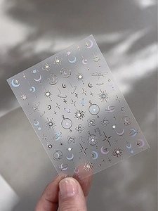 Dettaglio di adesivi per nail art con stelle e lune dorate e accenti blu celestiale