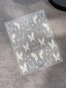 Detailed close-up of iridescent butterfly nail art stickers with white decorative lines