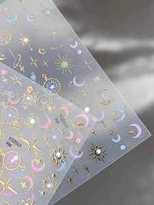 Dettaglio di adesivi nail art dorati con motivi celesti di stelle e luna pastello