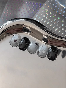 Détail de faux ongles Y2K faits main noirs et argentés avec étoiles sur plateau métal