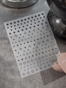 Vue détaillée d'autocollants pour ongles étoiles noires aux formes variées sur transparent