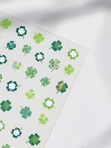Détail d'autocollants pour ongles trèfle avec textures pailletées et motifs de feuilles