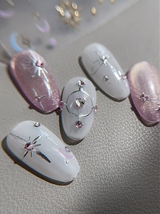 Vista macro di unghie press-on lavanda cat-eye con linee metalliche argentate e strass