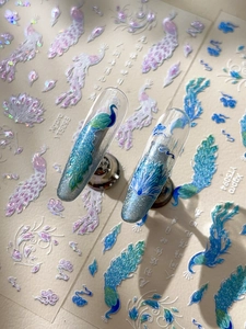Detail of peacock feather nail stickers with ancient calligraphy and sparkling glitter