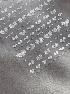 Makro-Detail von 3D-Präge-Herz-Nagelaufklebern in Silber mit LOVE ME und KISS ME Text