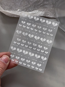 Detail von silbernen Glitzer-Herz-Nagelaufklebern mit LOVE ME Schriftzug auf Folie