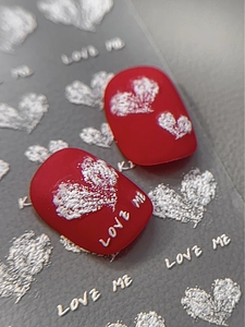 Makro-Detail von mattrotem Nagelaufkleber mit weißem Herzmuster und LOVE ME Schriftzug