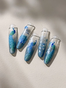 Detailed view of peacock feather nail art featuring blue gradients and calligraphy accents