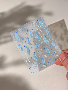 Macro view of peacock feather nail stickers with glitter finish and elegant cloud motifs